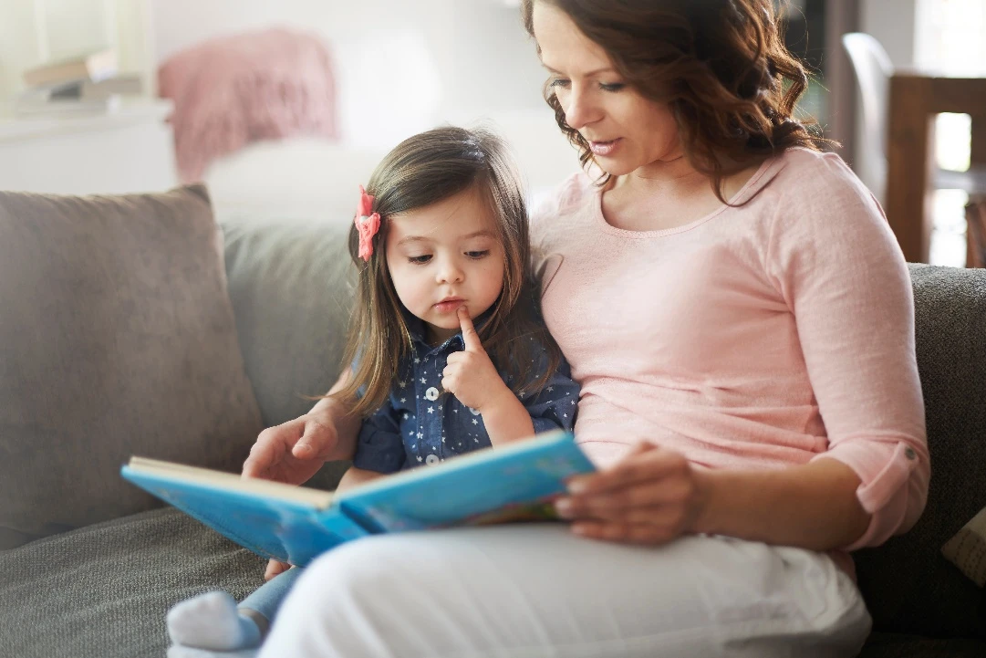 Parent and young child sitting together on a couch, reading a book.