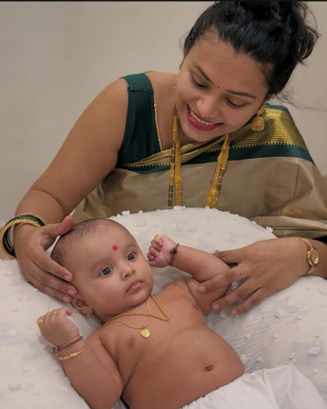 A mom lovingly smiling at her baby boy Ekaaksh, who is lying on a soft white cushion